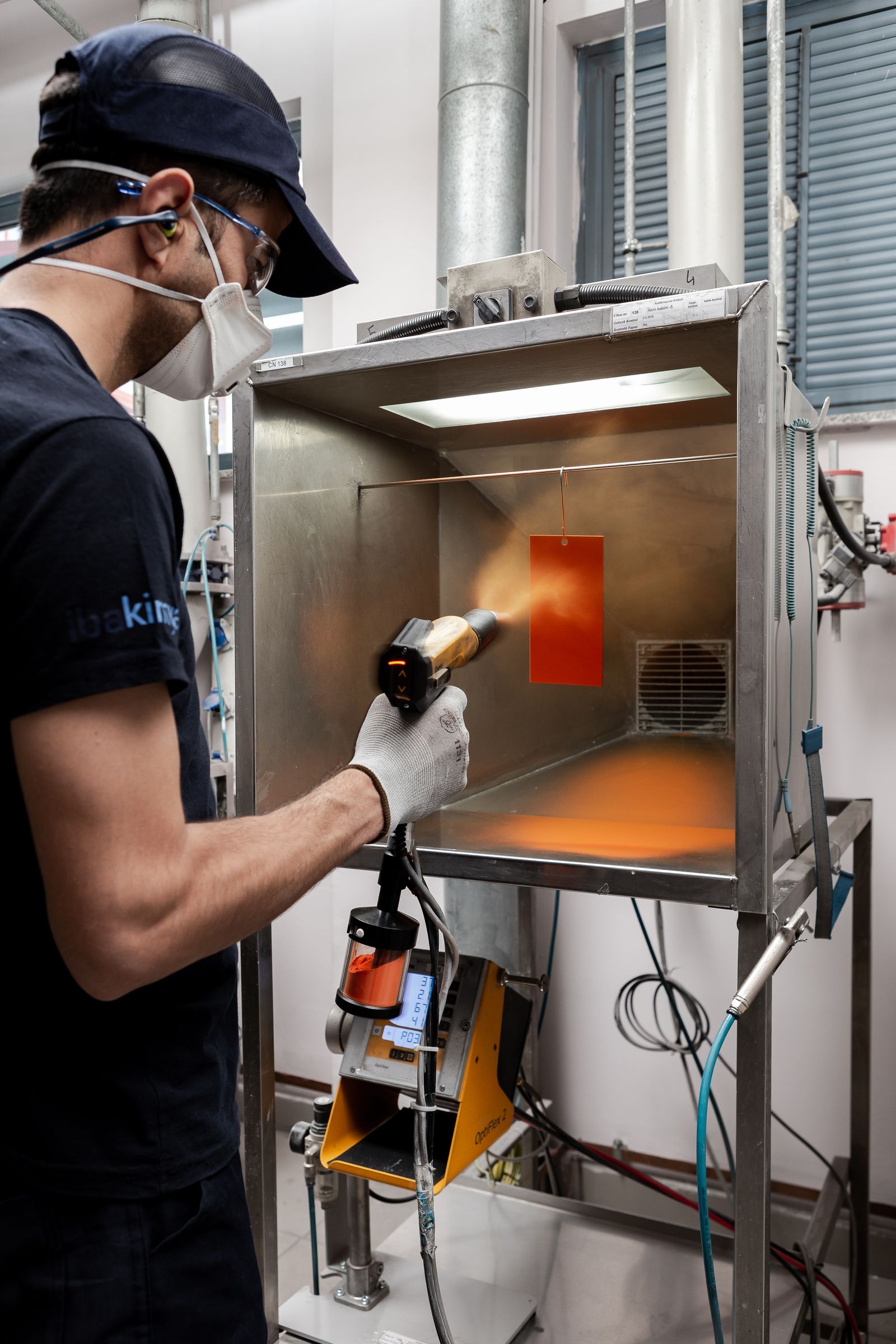 Ein Prüfblech wird in der Laborkabine von IBA Kimya elektrostatisch mit Pulverlack beschichtet